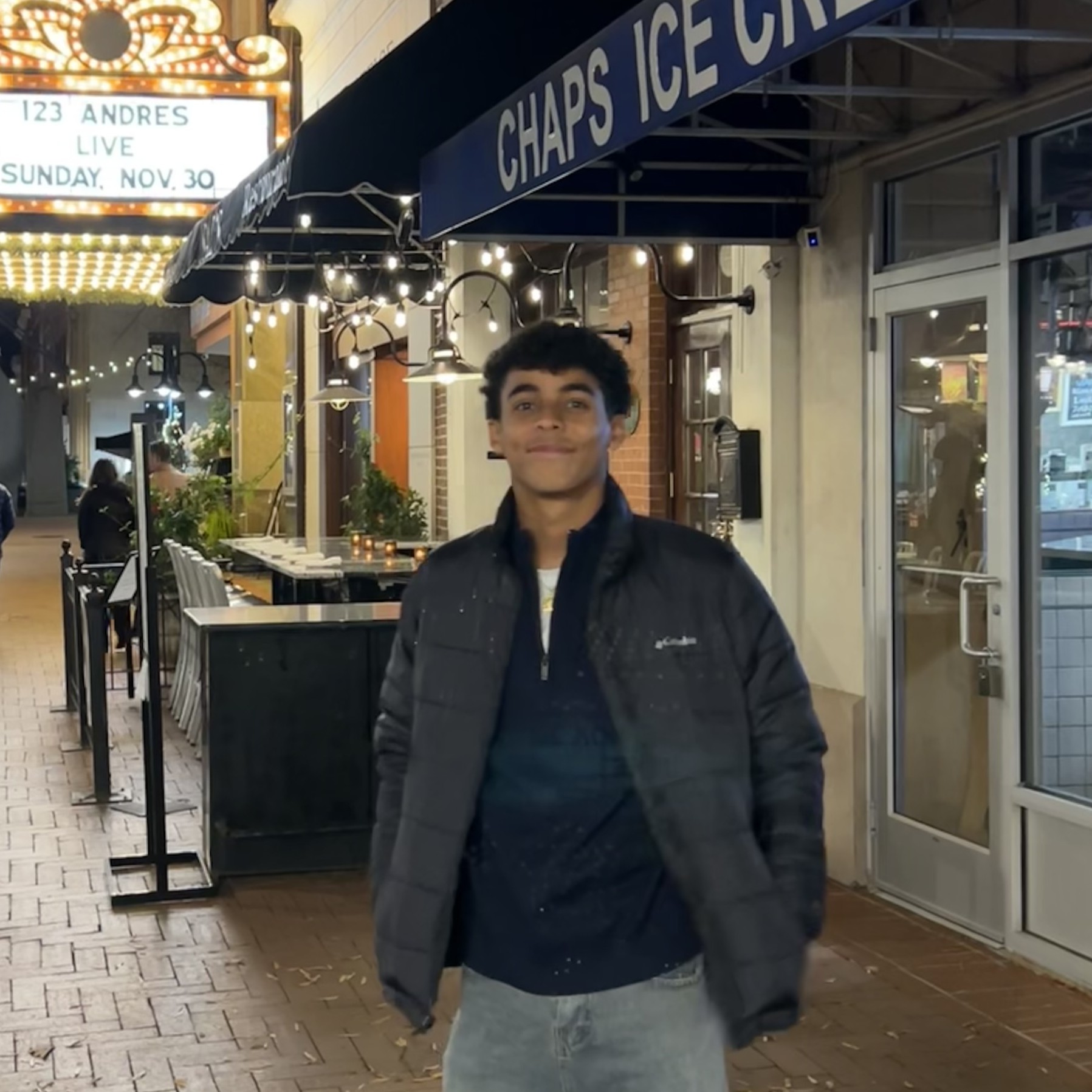 Young man standing outside an ice cream shop at night under string lights.