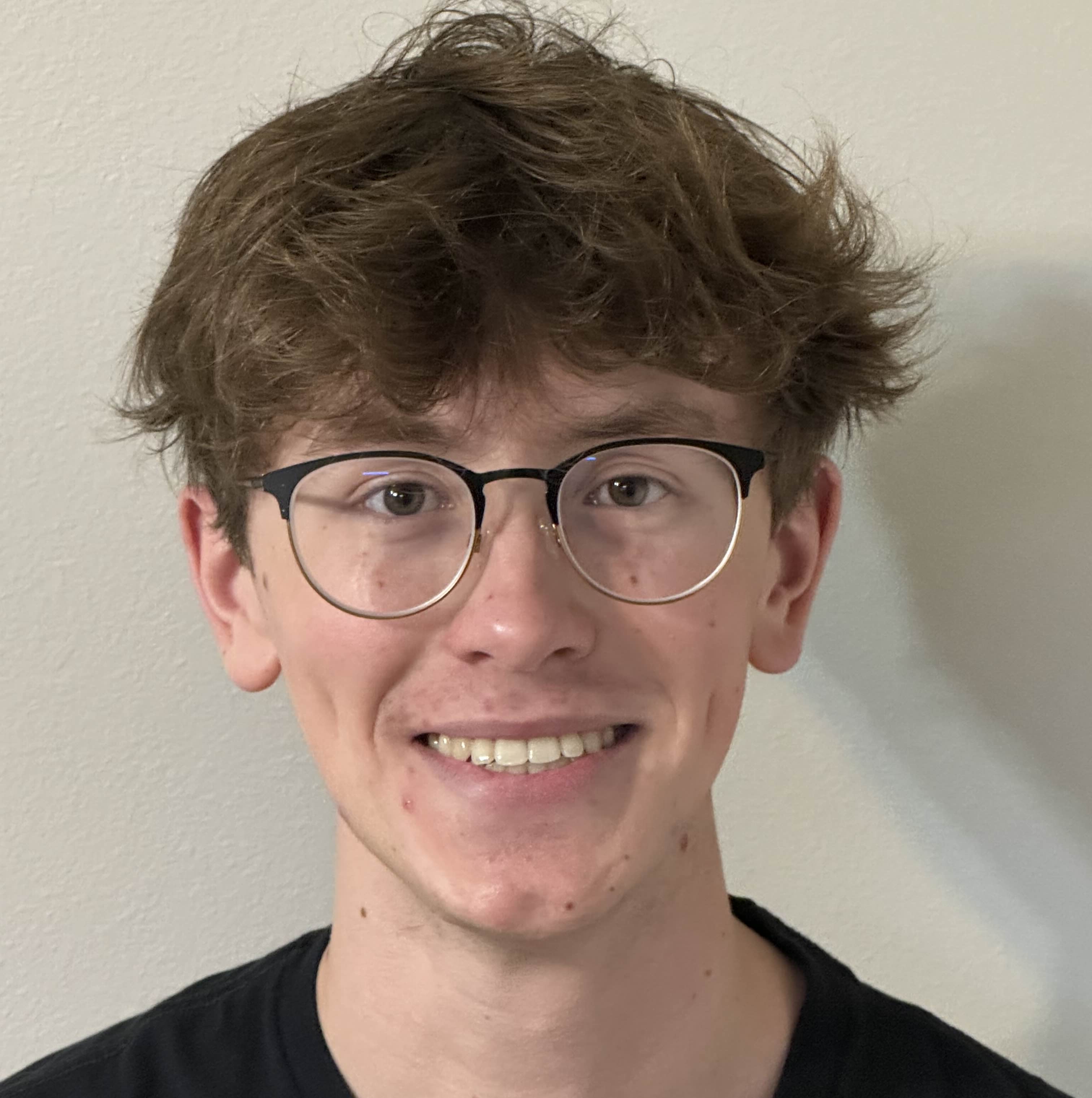 Smiling person wearing glasses, with messy hair and a neutral background.