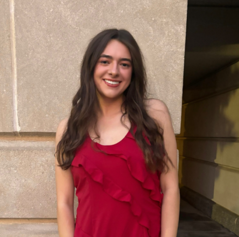 Smiling person in a red, ruffled dress standing against a light stone wall.