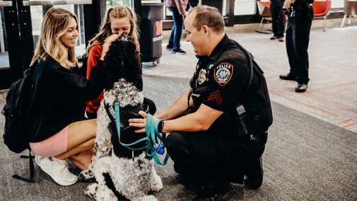 Two students meet the University Police Department’s Sergeant Conradt and therapy dog Cash in the Nebraska East Union on National Coffee with a Cop Day.