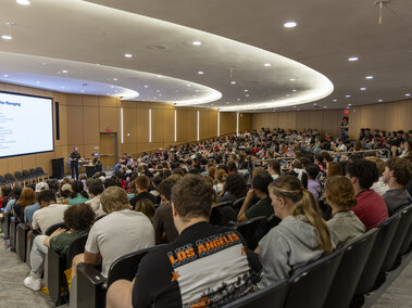 A large auditorium filled with students listening to a presenter.