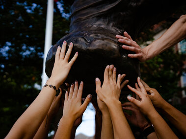 The hands of students touching the foot of the bronze mammoth sculpture by Morrill Hall.
