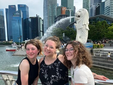 Three students posing in front of a Singaporean Merlion. The Merlion is the official mascot of Singapore. It is depicted as a mythical creature with the head of a lion and the body of a fish.
