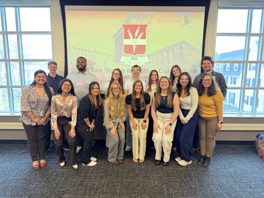 Tau Sigma initiates standing together in front of projected Tau Sigma Logo.